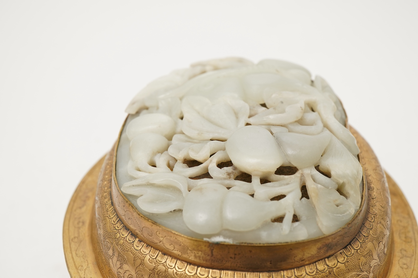 A Chinese pale celadon jade oval plaque, 17th/18th century, mounted on a late Qing gilt copper jar